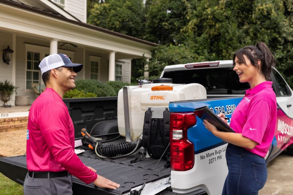Two Mosquito Authority team members stand near a truck and discuss something.